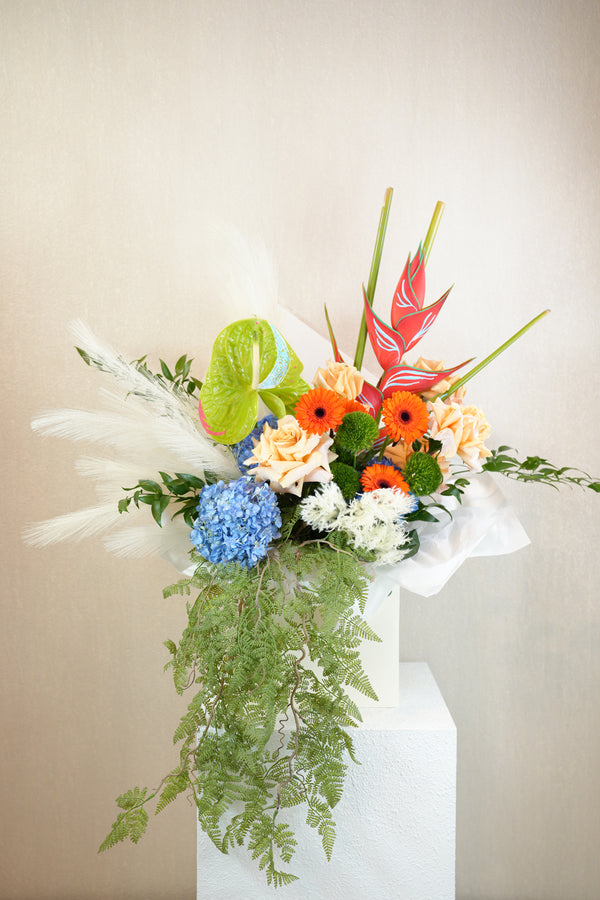 Colorful floral arrangement with greenery on a white pedestal against a beige background