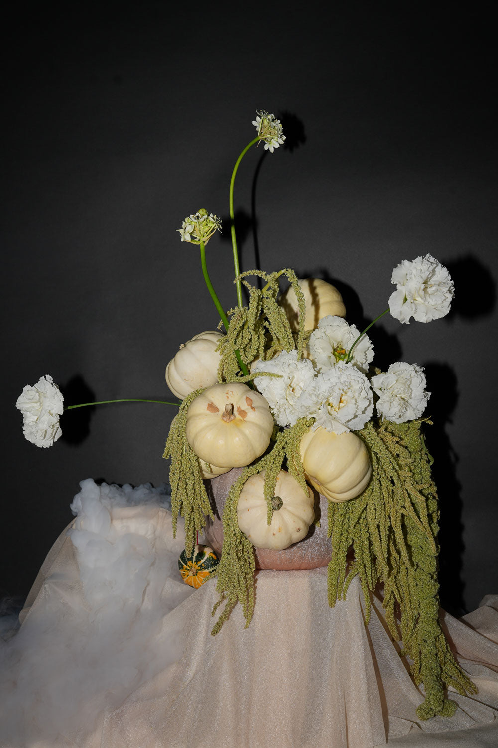 Decorative arrangement of white flowers and small pumpkins on a dark background,perfect for center table this halloween, curated by amicis flower shop