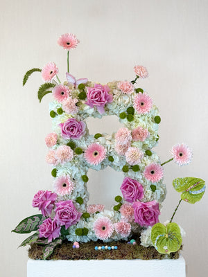 Floral letter 'B' made of pink, purple, and green flowers on a white background
