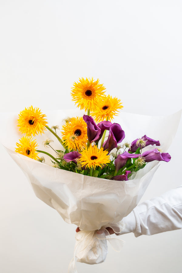 A striking harmony of sunshine yellow and regal purple, Golden Amethyst is a hand-tied bouquet that captures both warmth and sophistication. Bold yet balanced, this arrangement is a radiant expression of joy, creativity, and timeless charm by amicis flower shop