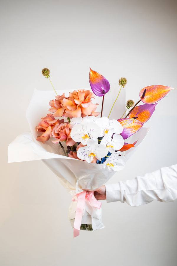 A dreamy fusion of peach, purple, and vibrant orange hues, Orchid Mirage features exotic orchids nestled among lush blooms. This hand-tied bouquet is a radiant blend of elegance and boldness—crafted to enchant, inspire, and leave a lasting impression flower bouquet made by amicis