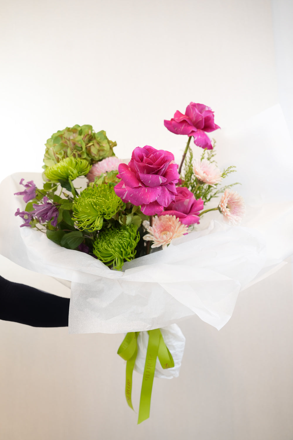 Bouquet of pink and green flowers with a white wrap and green ribbon on a light background