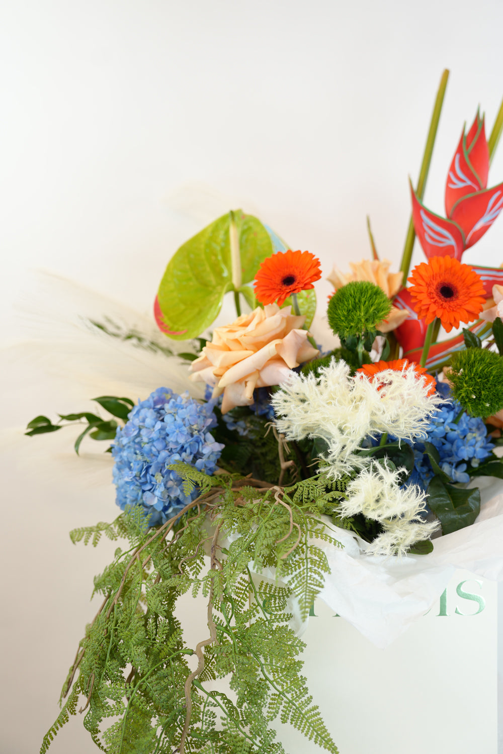 Colorful floral arrangement with greenery on a white pedestal against a beige background