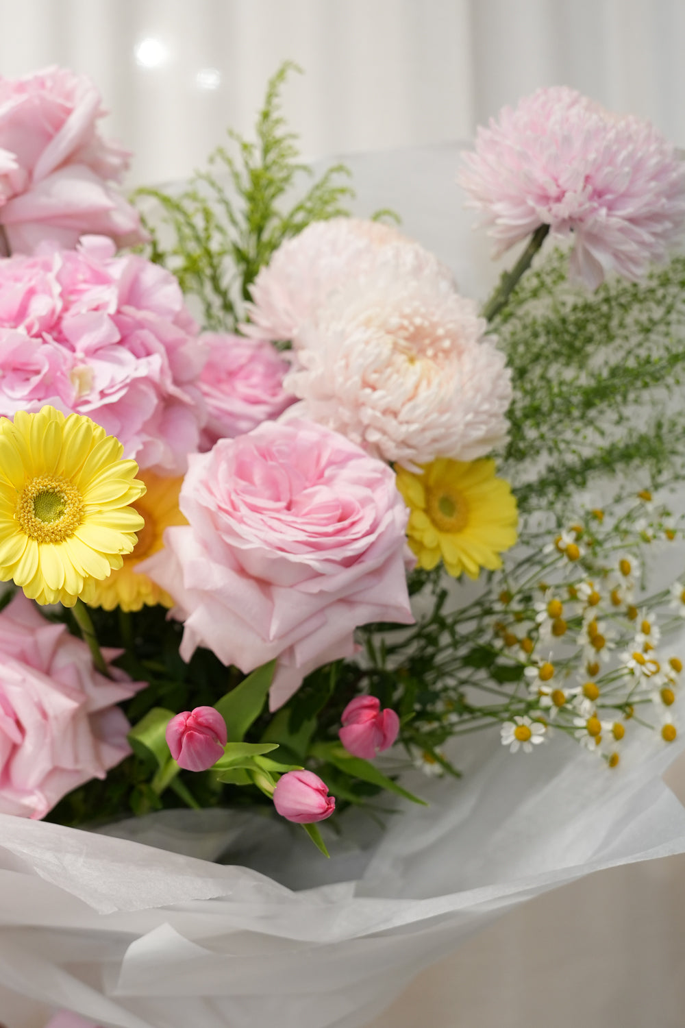 Bouquet of flowers by amicis flower shop held by a person against a white curtain