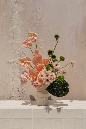 Seraphina - peach anthuriums, blush hydrangeas, and pink spiky gerberas with green foliage in a textured cream ceramic vase by Amicis