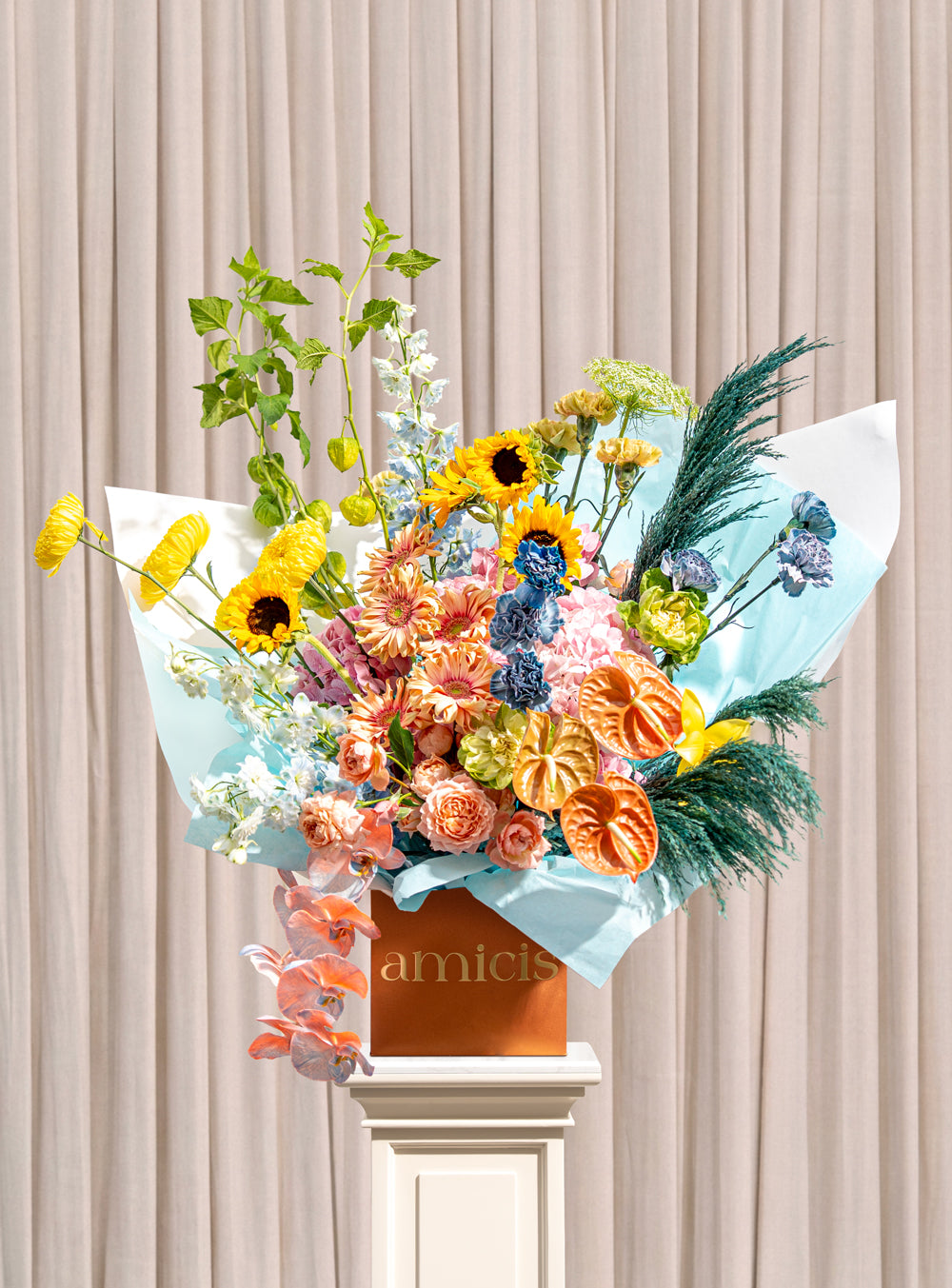 Gardenia peach and blue arrangement with sunflowers, blue delphinium, peach garden roses, copper anthurium and cascading orchids in a copper Amicis box