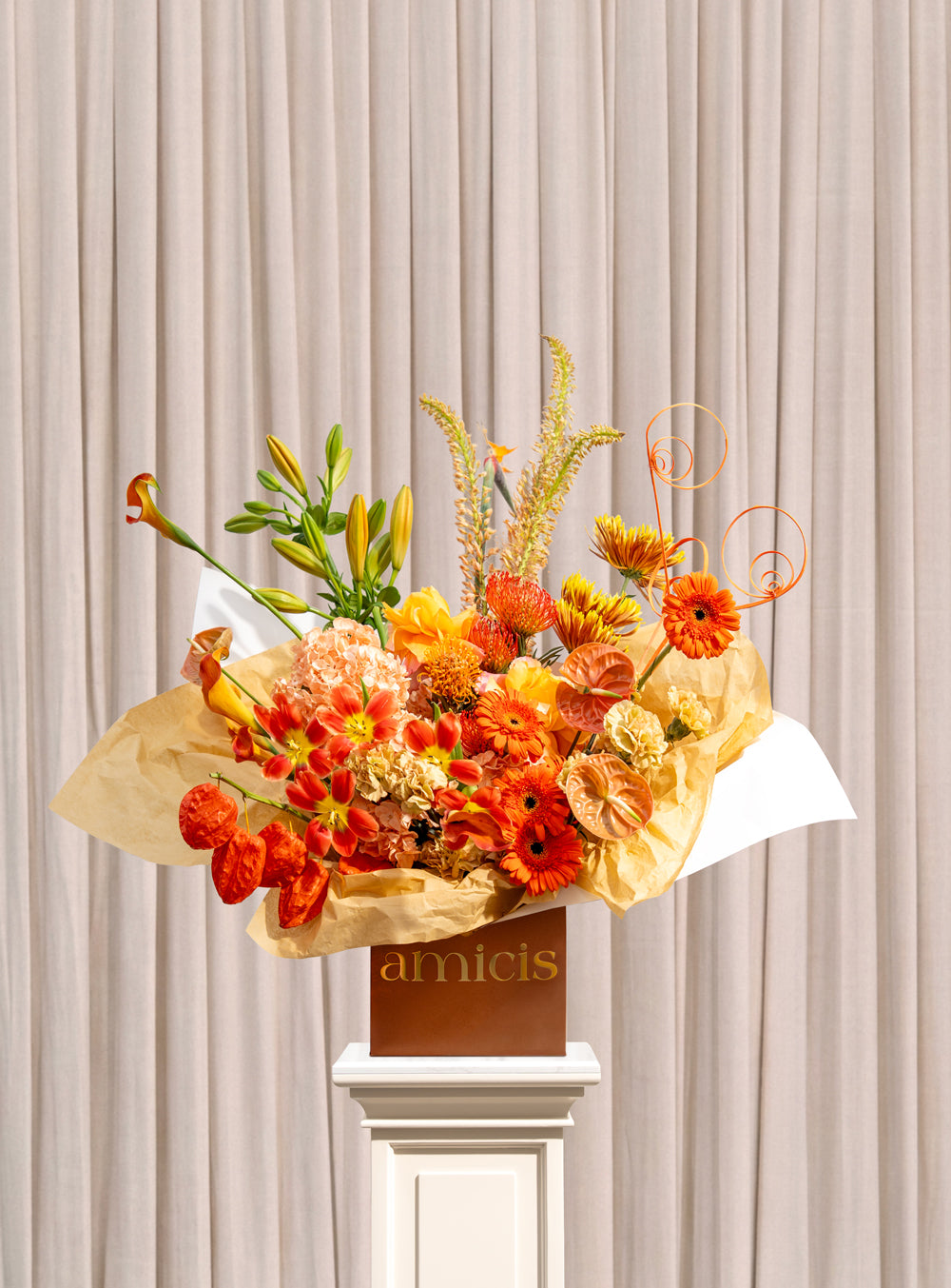 Laurel burnt orange arrangement with orange gerbera, dahlias, lily buds, apricot hydrangea and physalis lanterns in a copper Amicis box
