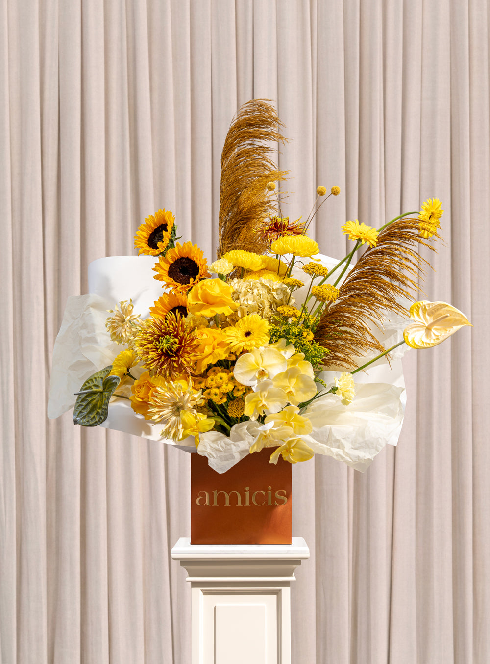 Solstice golden arrangement with sunflowers, yellow roses, chrysanthemums, craspedia and gold pampas grass in a copper Amicis box