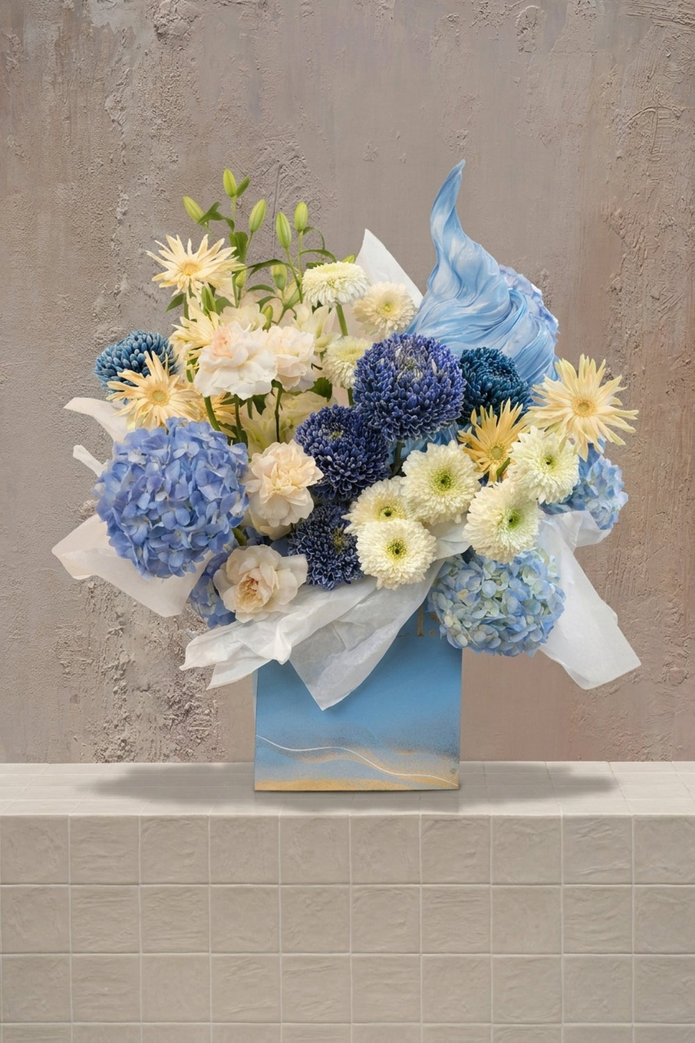 Amoré / 17 - light blue hydrangeas, deep blue, cream & pale yellow chrysanthemums, white lilies, and pale peach carnations in a blue gift box with white tissue by Amicis