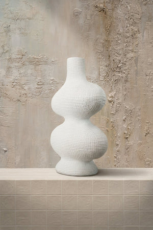 Ceramic Curve - a sculptural white textured ceramic vase with a unique double-bulb shape, presented on a beige tiled surface by Amicis