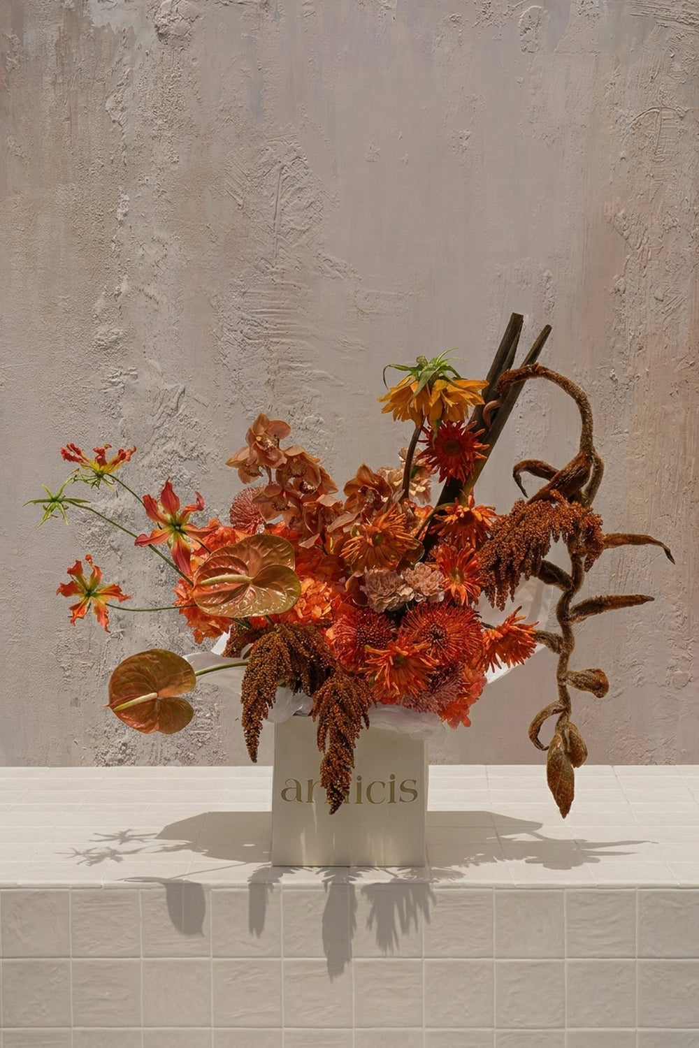 Tropic Azure - fiery orange gloriosa lilies, bronze anthuriums, rust orchids, amaranthus, and a curly vine in a cream ceramic vase by Amicis