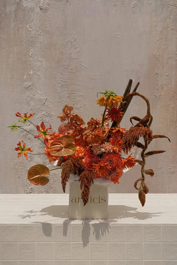 Tropic Azure - fiery orange gloriosa lilies, bronze anthuriums, rust orchids, amaranthus, and a curly vine in a cream ceramic vase by Amicis