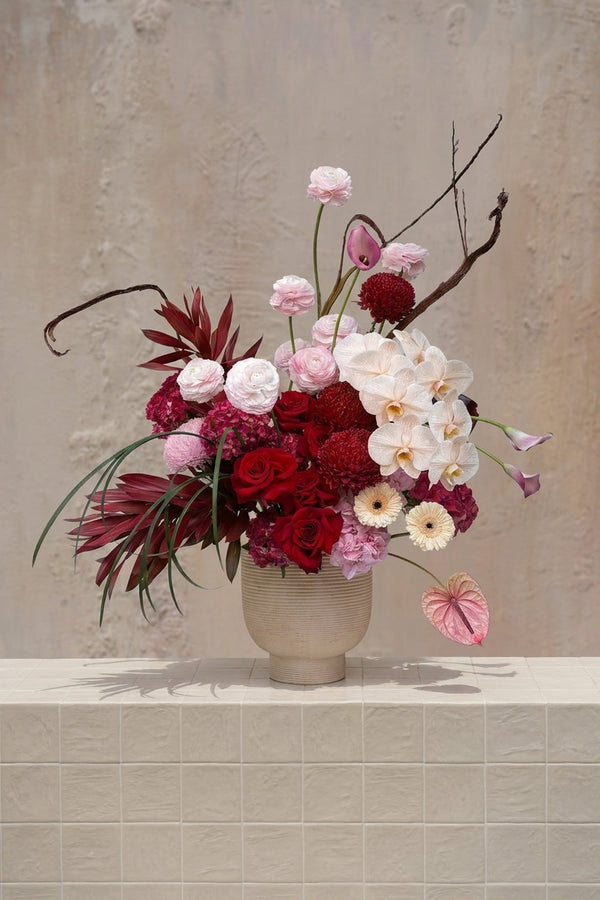 Cupid’s Crush - deep red roses, dahlias, blush ranunculus, cream orchids, pink anthurium, burgundy foliage in a ribbed vase by Amicis