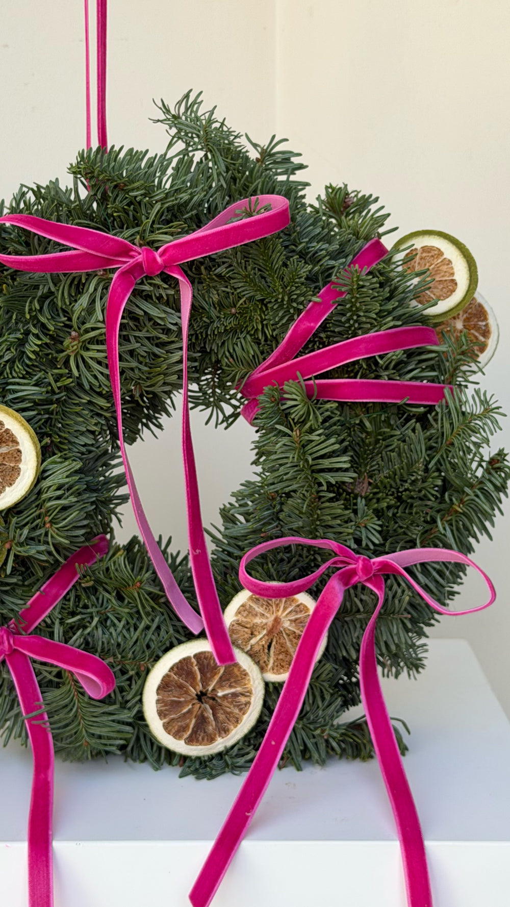 Sparkle Holidays 09 - deep green evergreen wreath adorned with dried citrus slices and deep pink velvet ribbons by Amicis