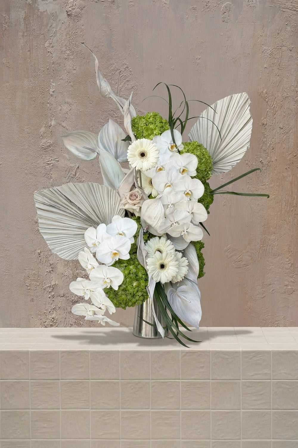 Dewdrop Garden - white orchids, gerberas, green hydrangeas, blush rose, and anthurium with dried palms in a silver vase by Amicis