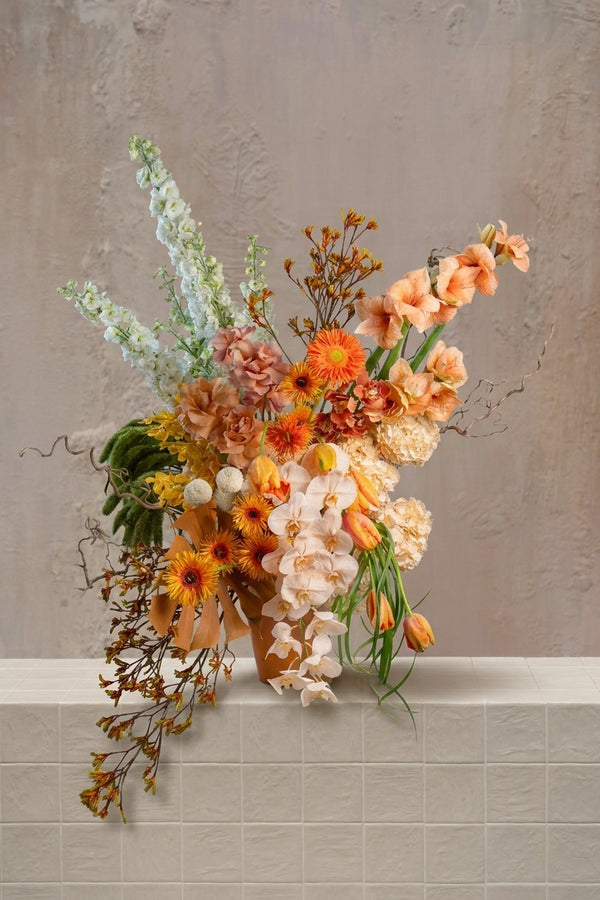 Engrande - vibrant peach, orange, and cream amaryllis, gerberas, orchids, and delphinium with green amaranthus in a terracotta vase by Amicis