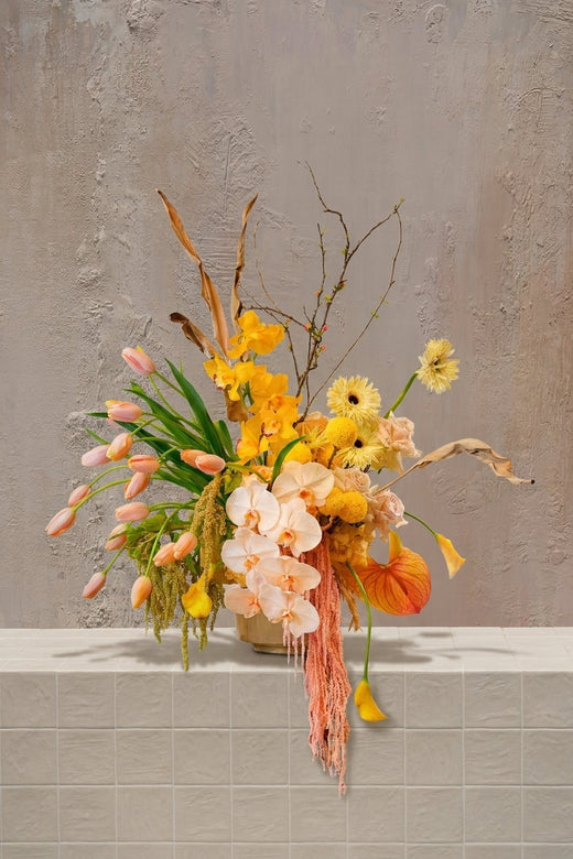 Feminine Orchard - peach tulips, yellow orchids, orange anthurium, yellow gerberas, and trailing