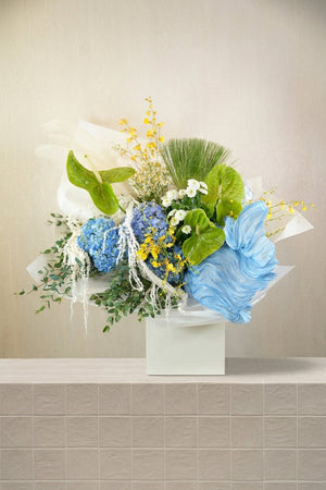 Jazz & Jasmine - blue hydrangeas, lime anthurium, yellow orchids, white amaranthus, and eucalyptus in a white box with blue fabric by Amicis