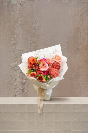 Scarlet Whisper - blush pink roses, peach ranunculus, and orange-red pincushion protea in a white wrapped bouquet with ribbon by Amicis.