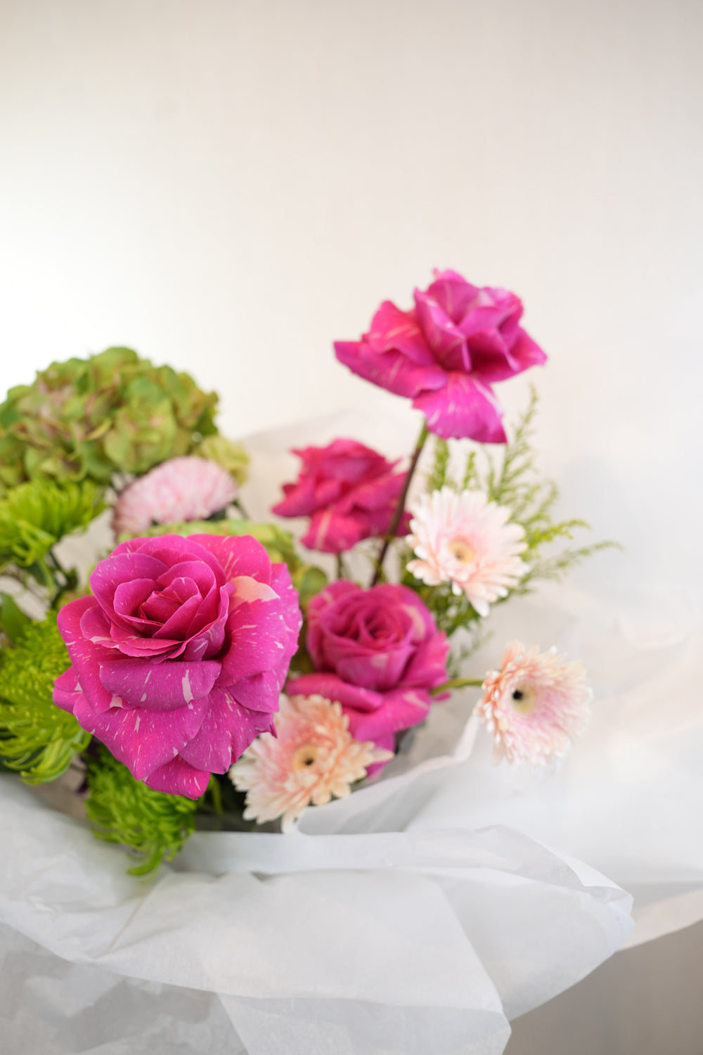 Bouquet of pink and green flowers with a white wrap and green ribbon on a light background