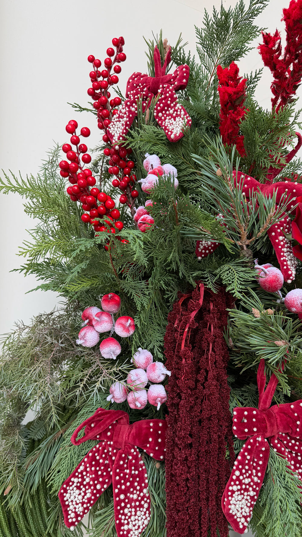 Sparkle Holidays 03 - deep red roses, berries, celosia, amaranthus, and evergreen in a white ceramic vase by Amicis