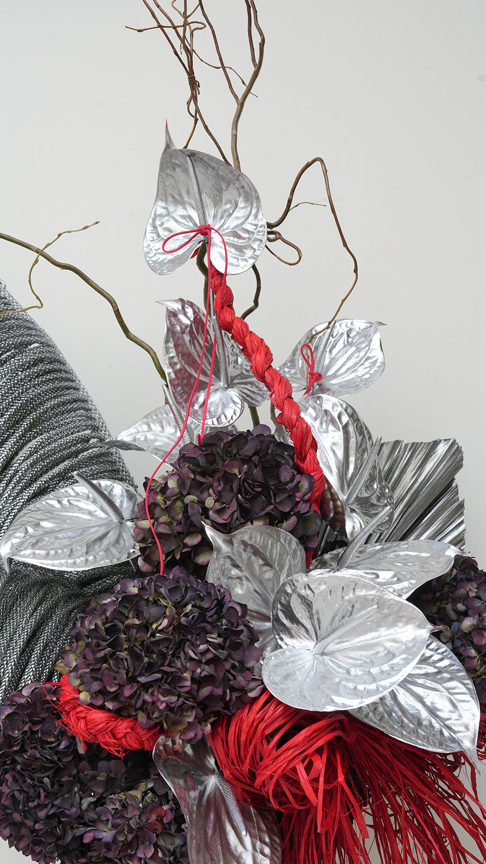 Sparkle Holidays 13 - silver anthurium, dark purple hydrangeas, red straw accents, and grey feathered palms in a silver vase by Amicis.