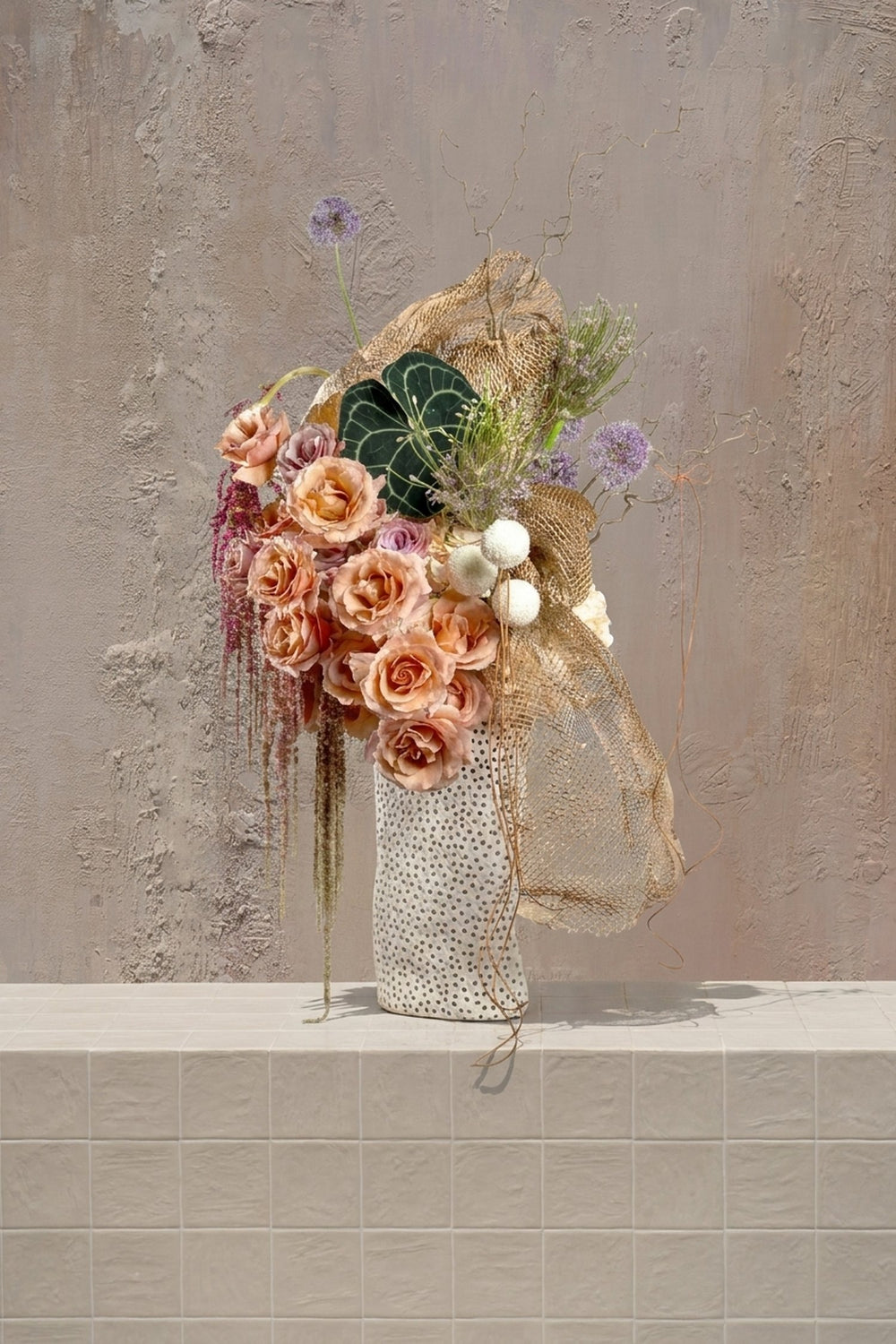 Honey Bee - peach roses, lavender alliums, amaranthus, anthurium leaf, and gold mesh in a polka-dot vase by Amicis