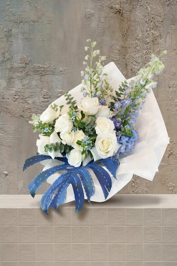 Blue jeans - white roses, blue hydrangeas, delphinium, and eucalyptus in a white wrapped bouquet with a blue leaf accent by Amicis.