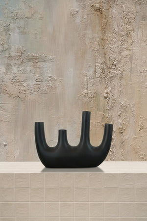 Line-Up Pipe - a luxury black multi-spouted ceramic vase on a beige tiled surface against a textured wall by Amicis