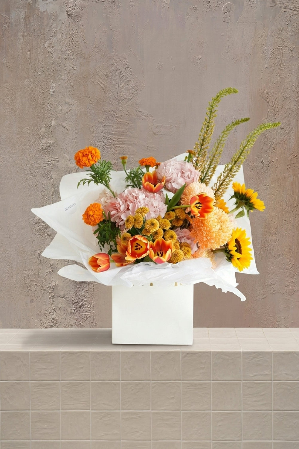 Sunset Glow - orange marigolds, yellow sunflowers, blush pink carnations, and red-orange tulips in a white gift box by Amicis