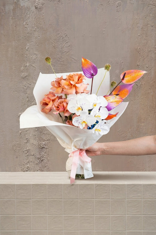 Orchid Mirage - white orchids, peach roses, purple-orange anthurium, and green alliums in a white