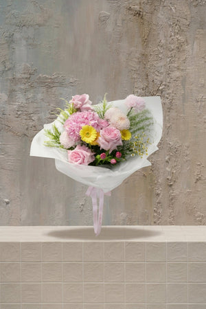 Evangeline - blush pink roses, pink carnations, yellow gerbera, white mums, and pink tulip buds with greenery in a white wrapped bouquet by Amicis.