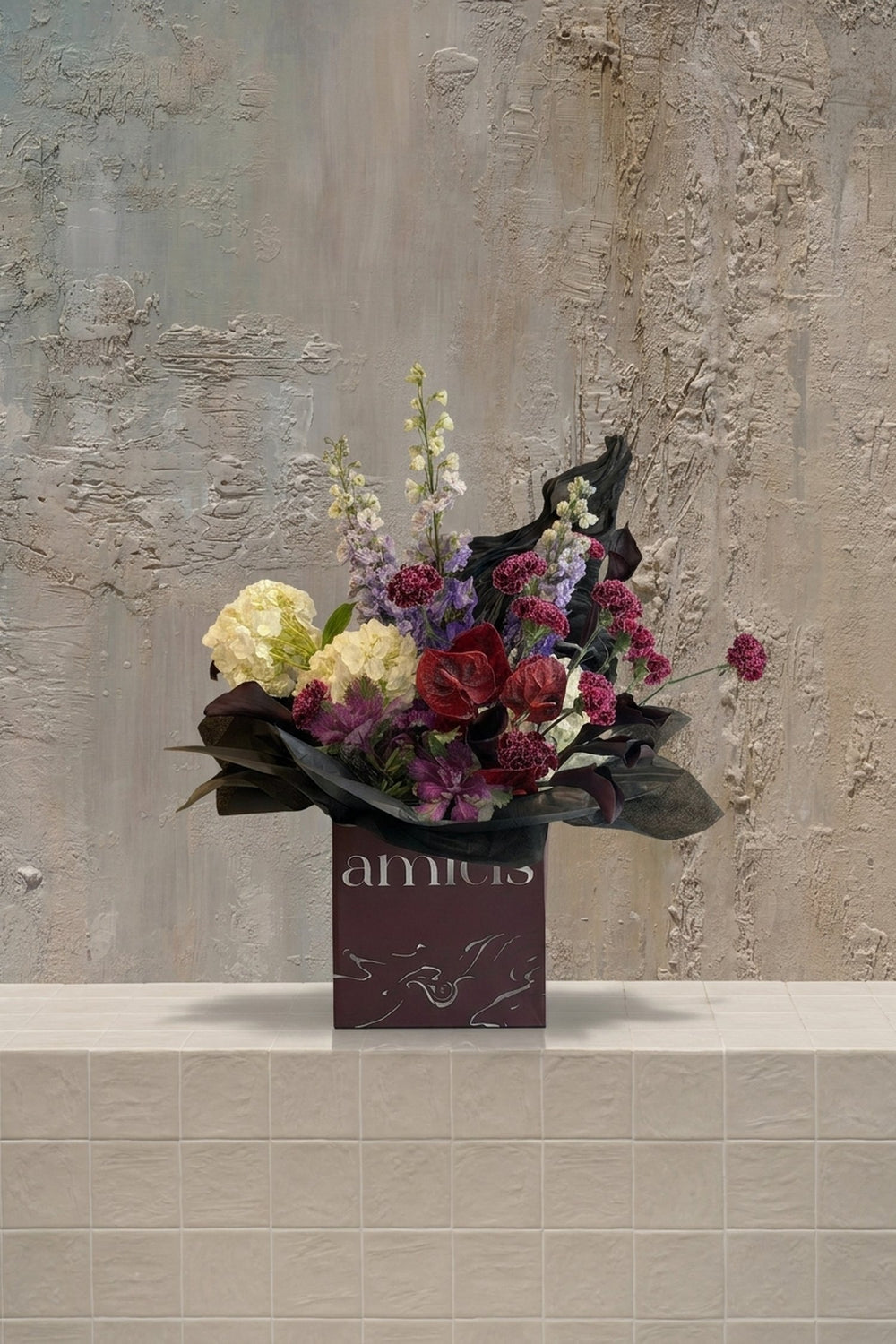 Rust & Velvet - cream hydrangeas, deep red roses, burgundy anthurium, lavender stock, and dark pink carnations in a burgundy floral box by Amicis.