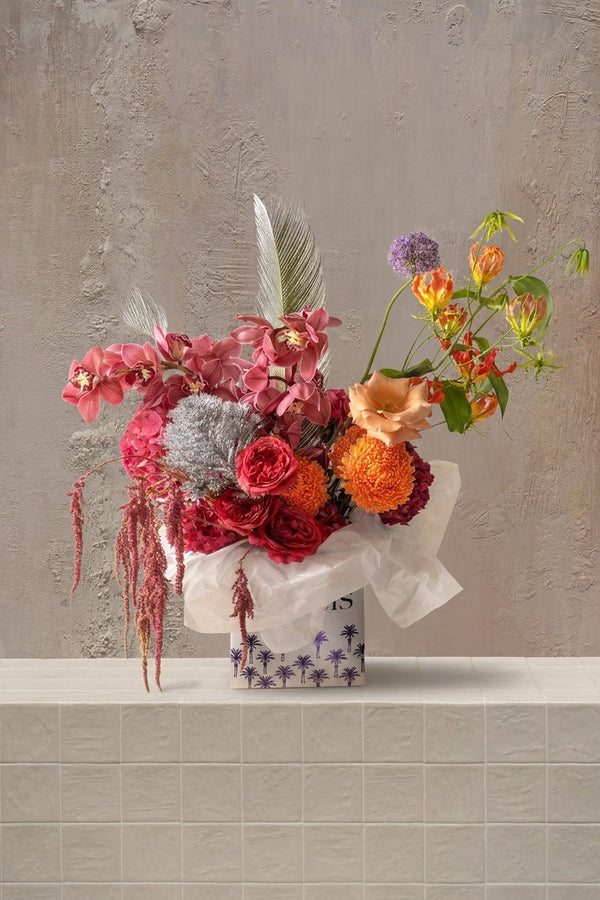 Sakinah Series - red roses, coral orchids, orange chrysanthemums, purple allium, and silver accents in a palm-print box by Amicis.