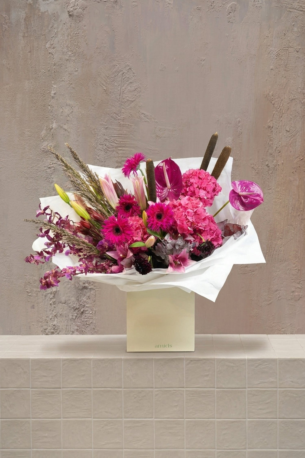 Sample - vibrant pink hydrangeas, anthurium, gerberas, and purple orchids with lilies in a white wrapped bouquet and cream gift box by Amicis