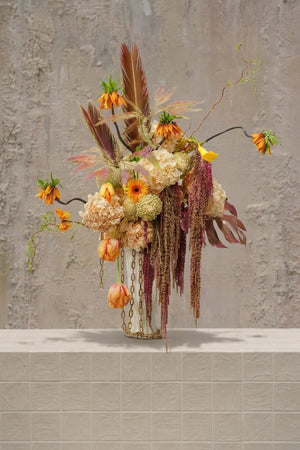 Seraphine - orange fritillaria, peach tulips, cream hydrangeas, and deep red amaranthus in a white ceramic vase with gold chain by Amicis