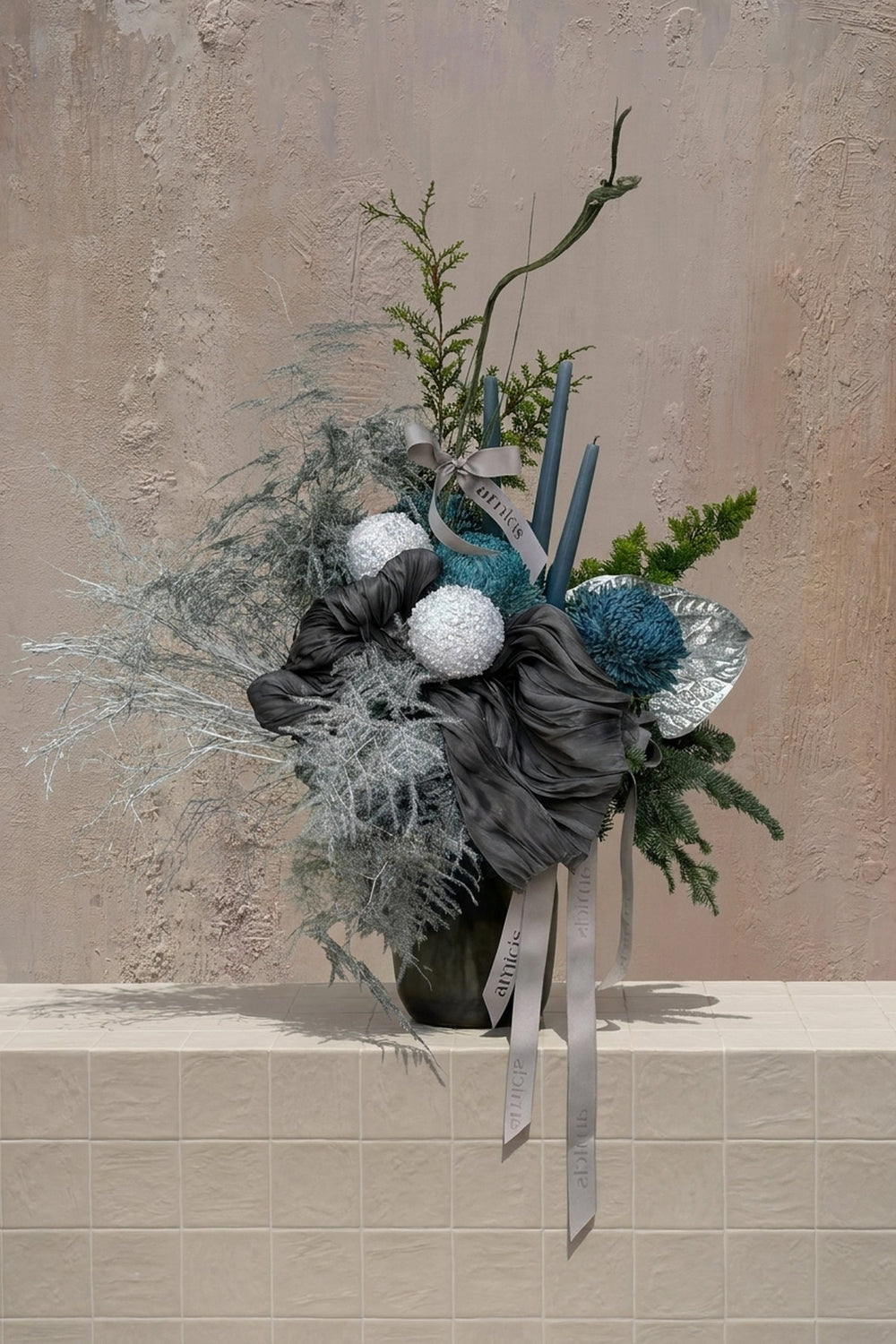 Sparkle Holidays 06 - silver foliage, dark green pine, white & teal hydrangeas, silver anthurium, and dark blue candles in a dark ceramic vase by Amicis