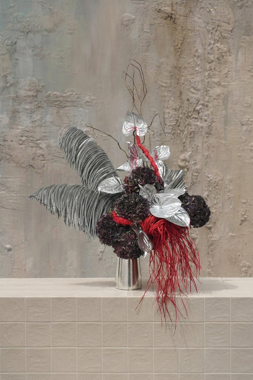 Sparkle Holidays 13 - silver anthurium, dark purple hydrangeas, red straw accents, and grey feathered palms in a silver vase by Amicis.