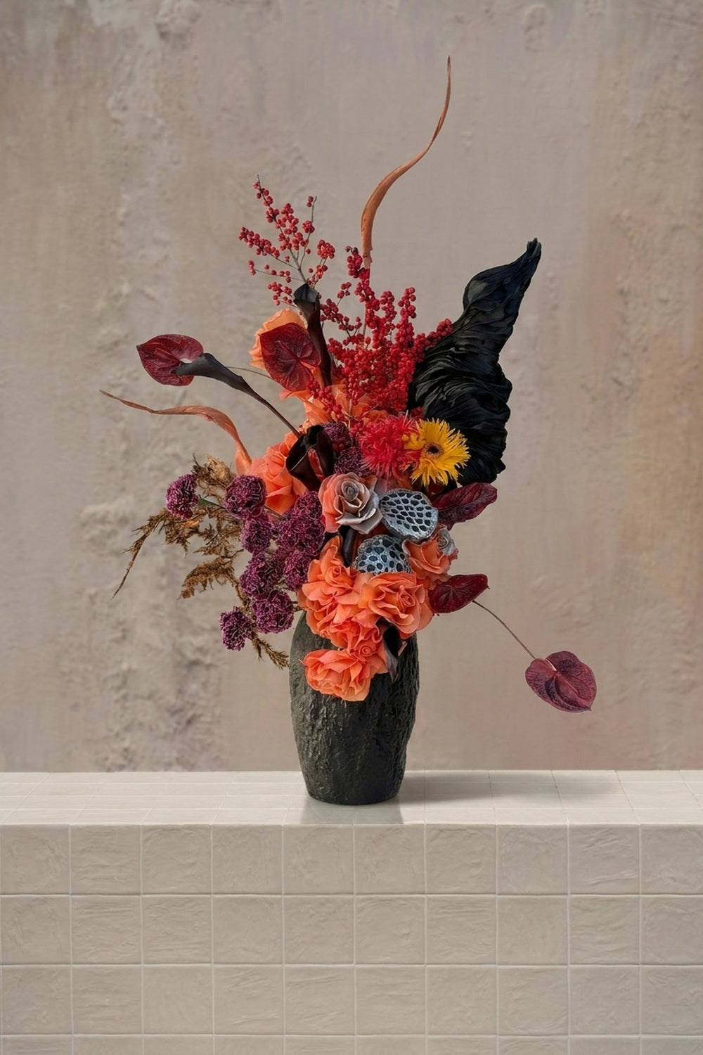 Statement - orange roses, deep red berries, black anthurium, yellow gerbera, and dried lotus pods in a black ceramic vase by Amicis