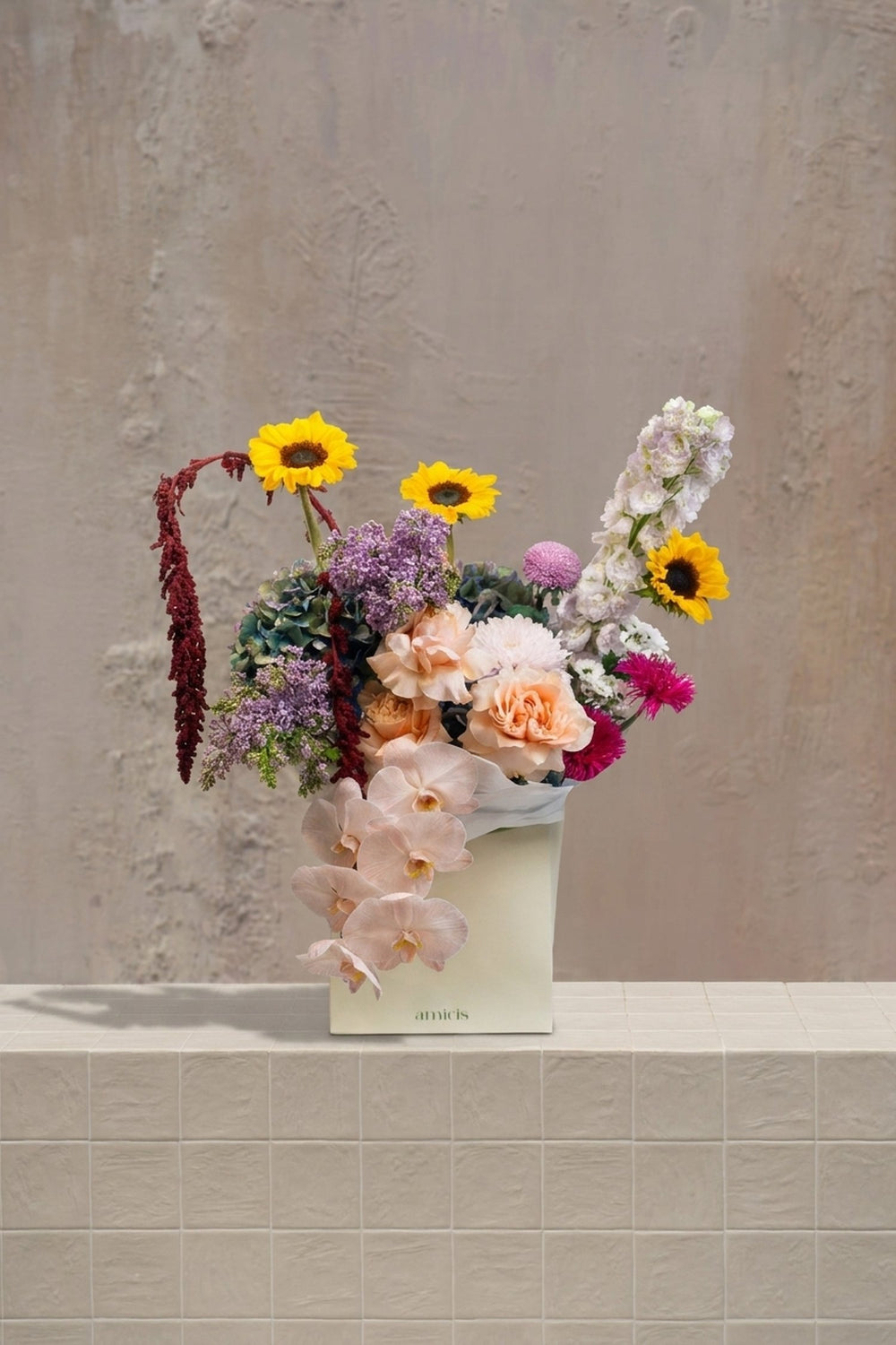 Sunlit-Symphony - yellow sunflowers, peach roses, blush orchids, lavender flowers, blue hydrangeas, and red amaranthus in a cream box vase by Amicis