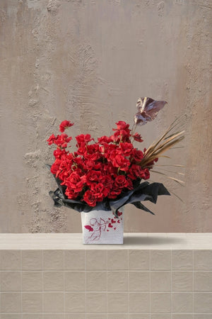 The Love Edit - deep red roses, dark burgundy anthurium, and golden grasses in a white box with cupid drawing and black wrap by Amicis