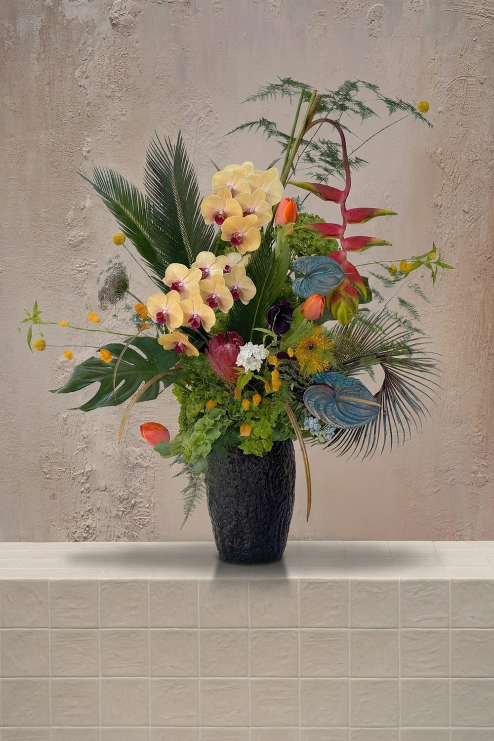 Tropical Parrot - yellow orchids, red heliconia, blue anthurium, orange tulips, and burgundy protea in a black textured vase by Amicis